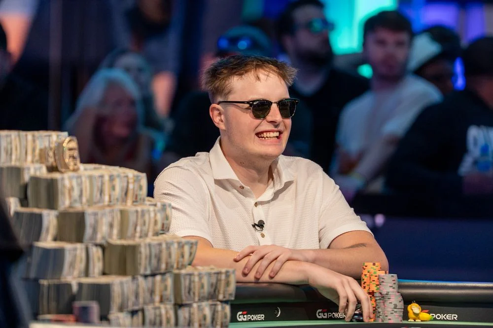 Poker player smiling at a televised final table beside stacks of chips
