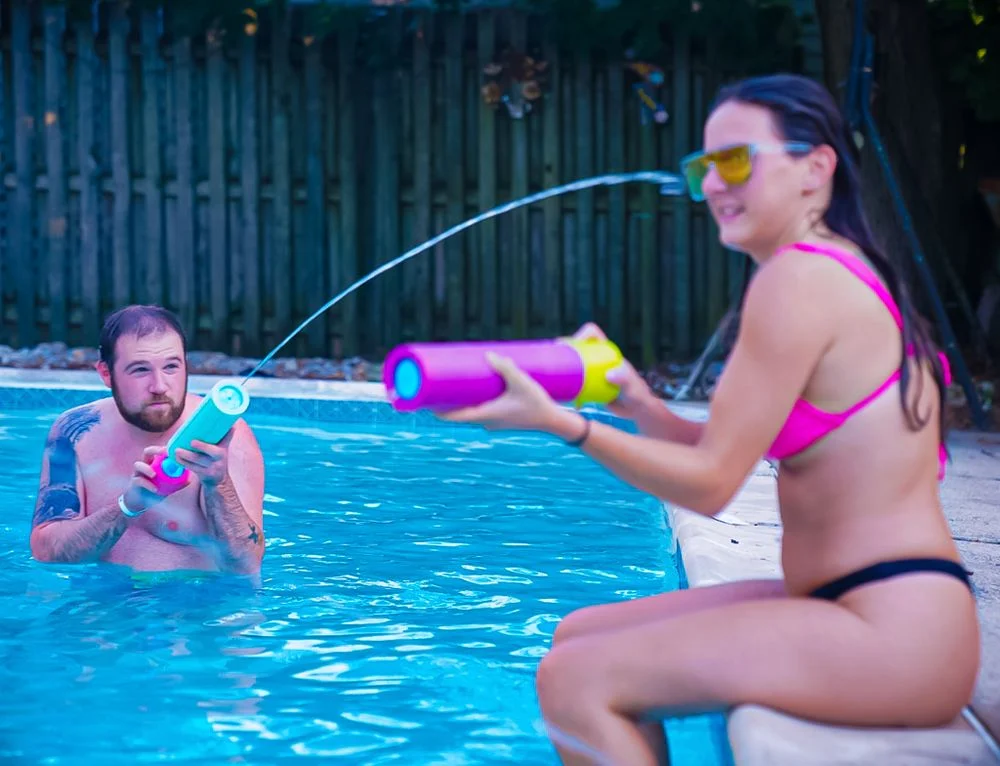 Friends share a playful poolside moment with colorful water blasters.