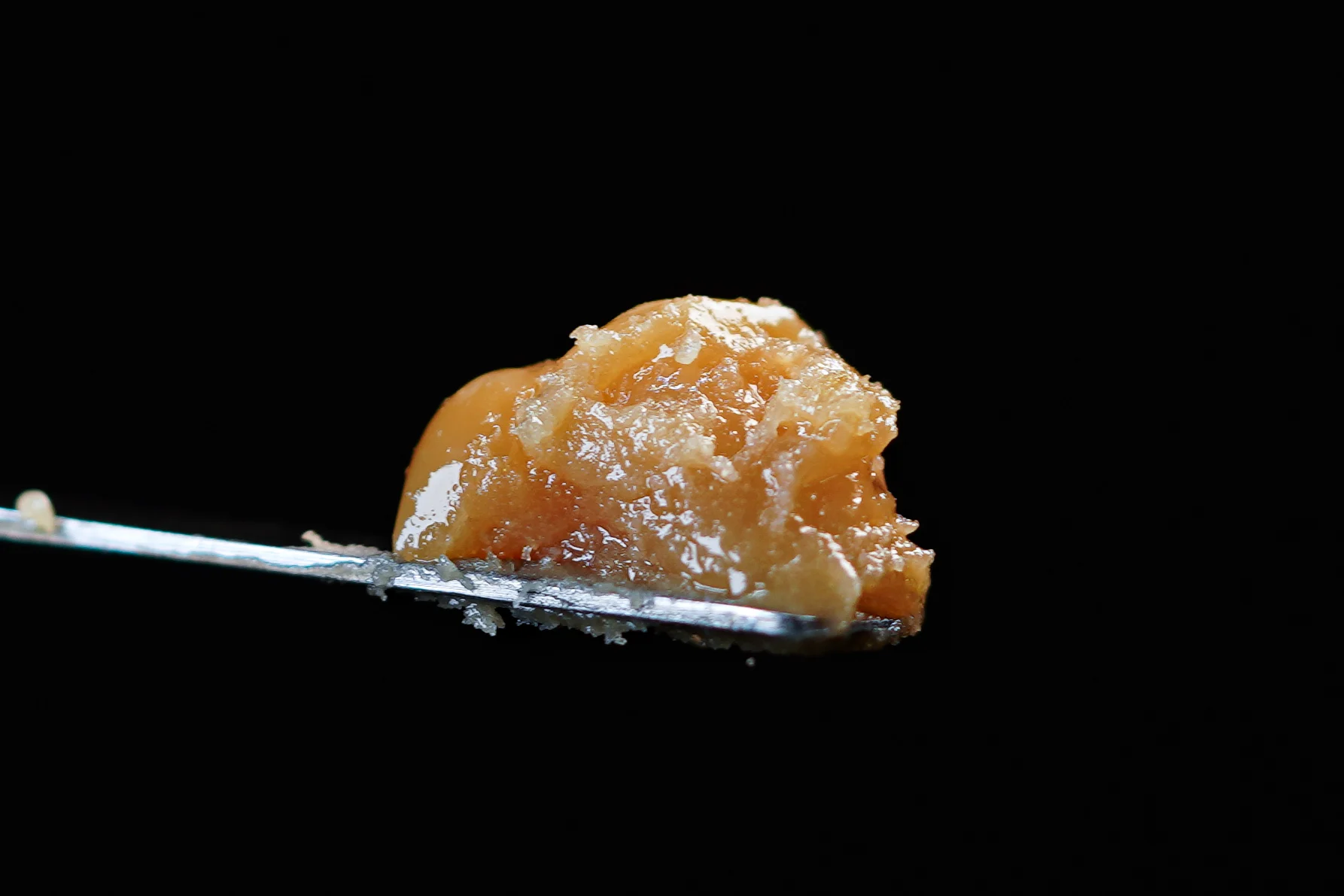 Amber cannabis concentrate sits on a metal dab tool against a black background.