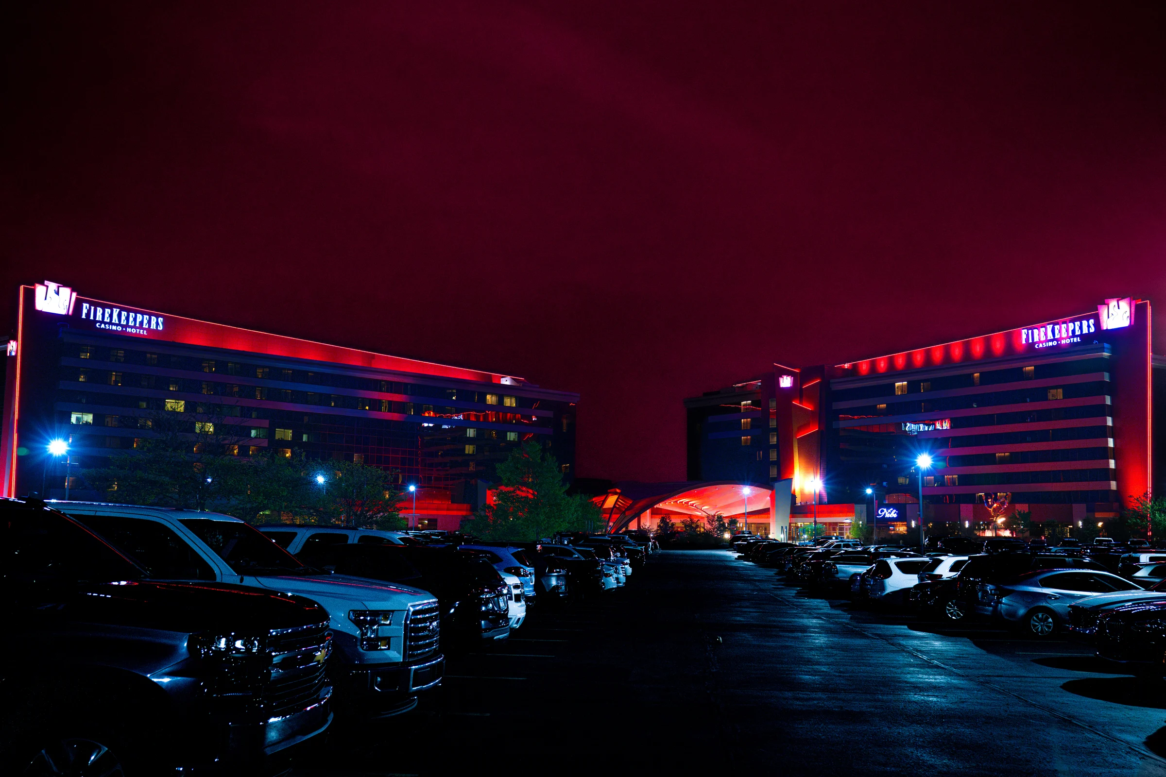 FireKeepers Casino Hotel glows red above a busy parking lot at night.