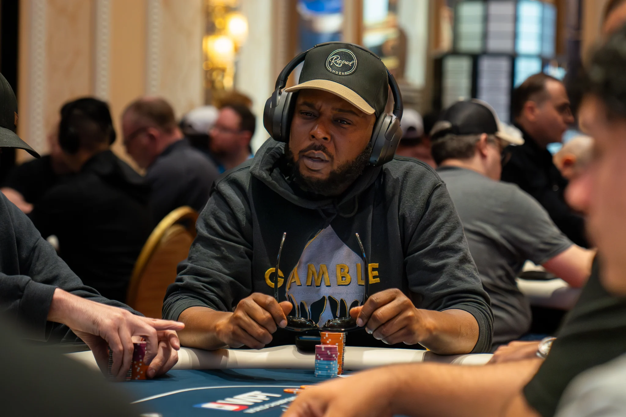 A focused poker player in headphones sits behind a stack of chips at a crowded tournament table.