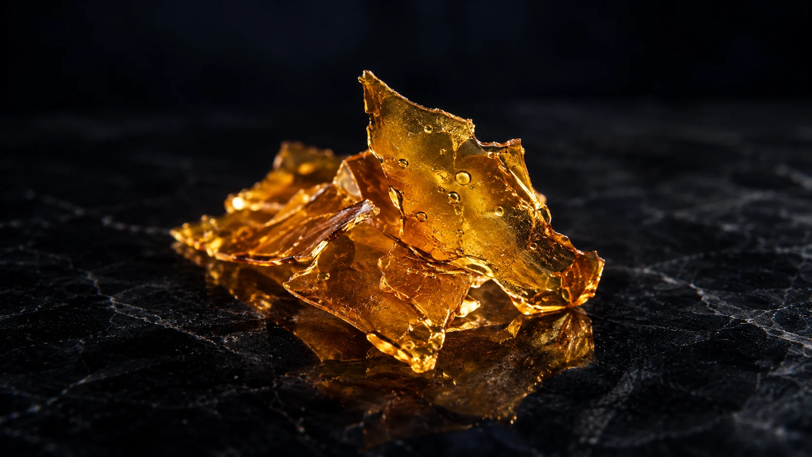 Golden cannabis concentrate rests on a black textured surface in a dramatic studio close-up.