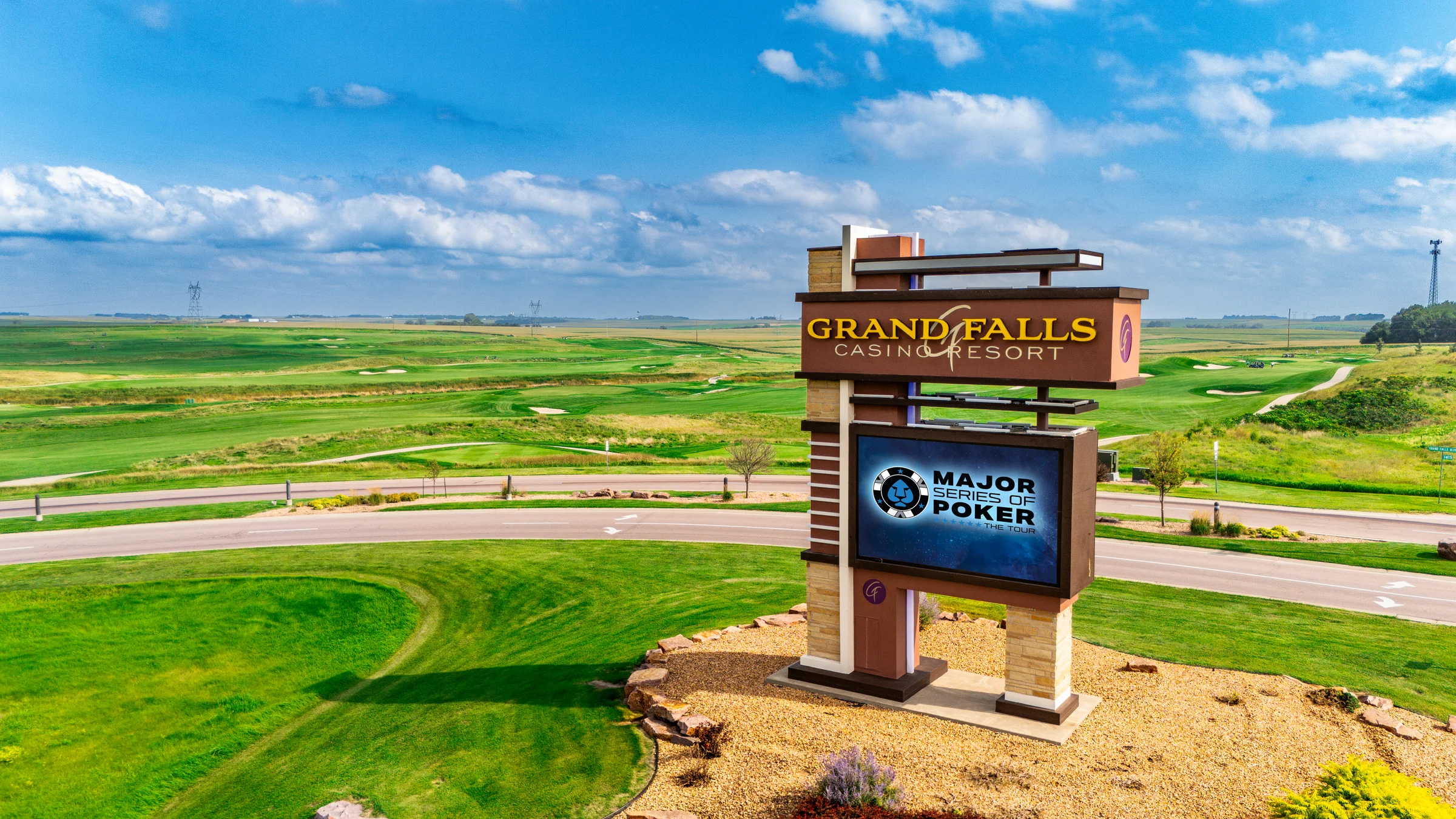 Grand Falls Casino Resort signage overlooks green fields under a bright blue sky.