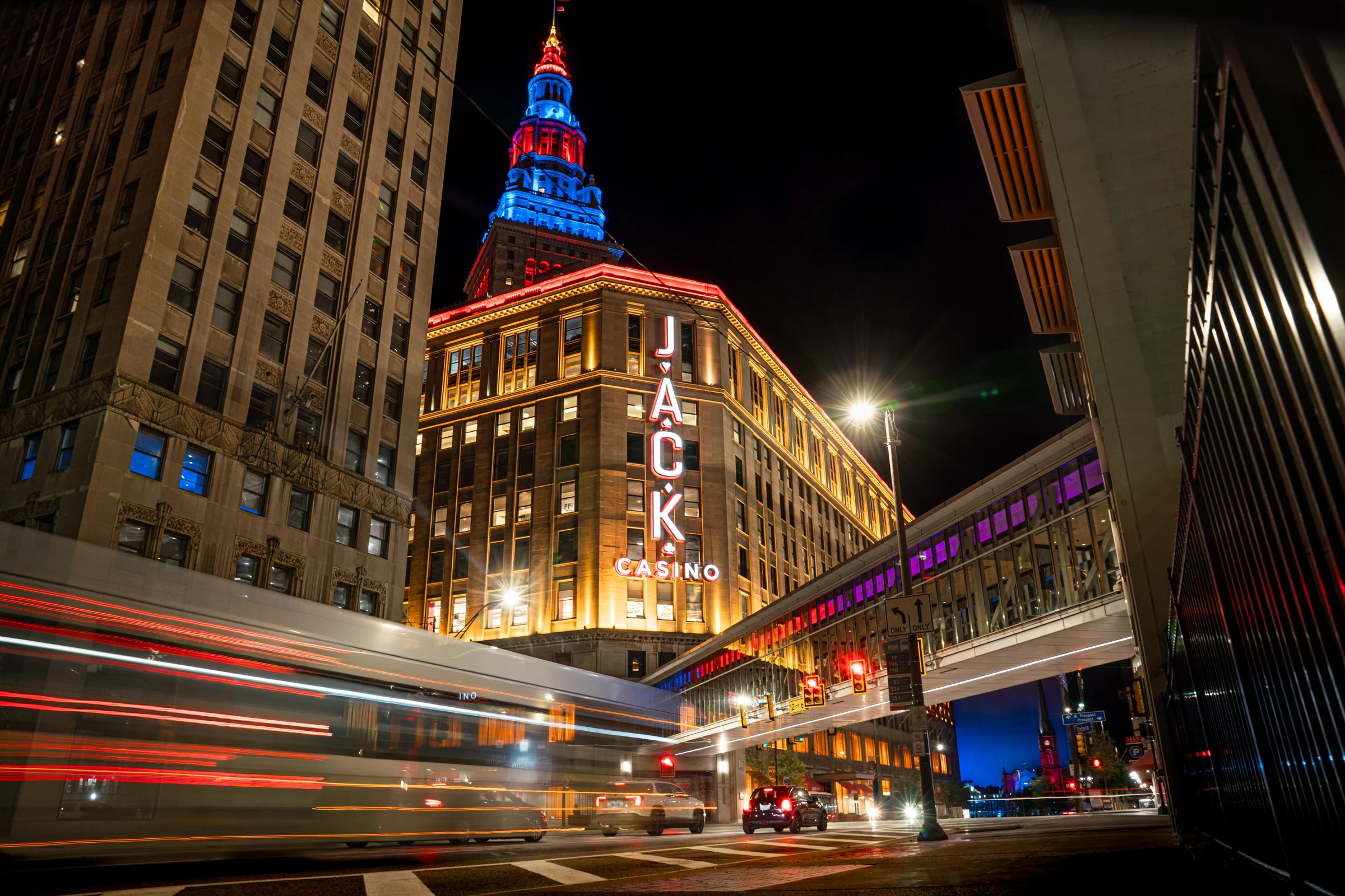 Light trails pass the illuminated JACK Casino building on a downtown street at night.