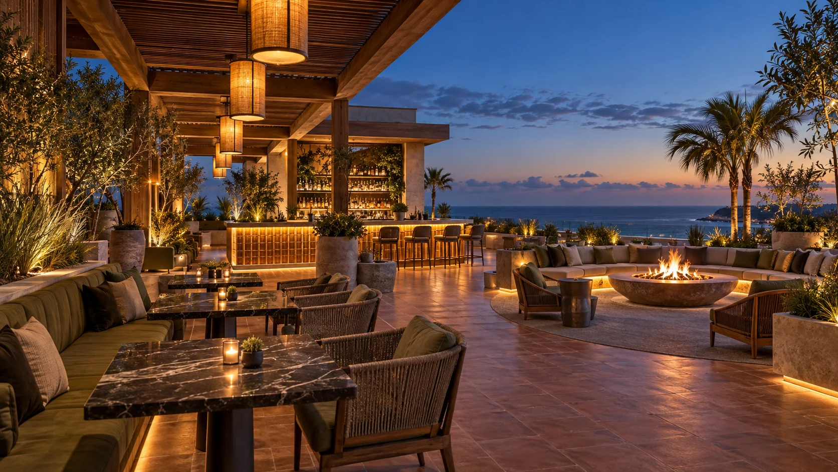 Open-air oceanfront resort restaurant with dining tables, a glowing bar and fire features at twilight.