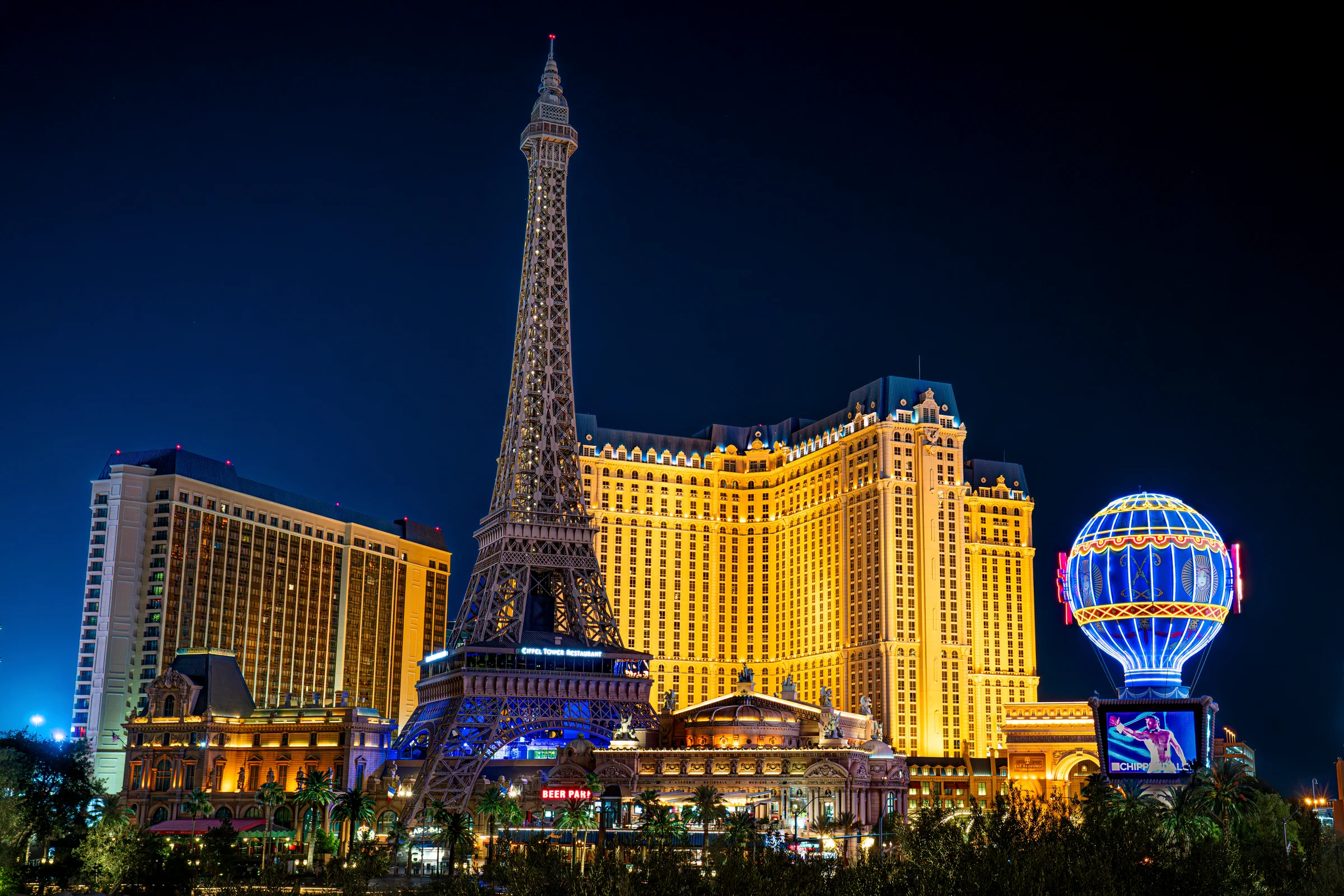 Paris Las Vegas glows at night with its Eiffel Tower and balloon signs illuminated.