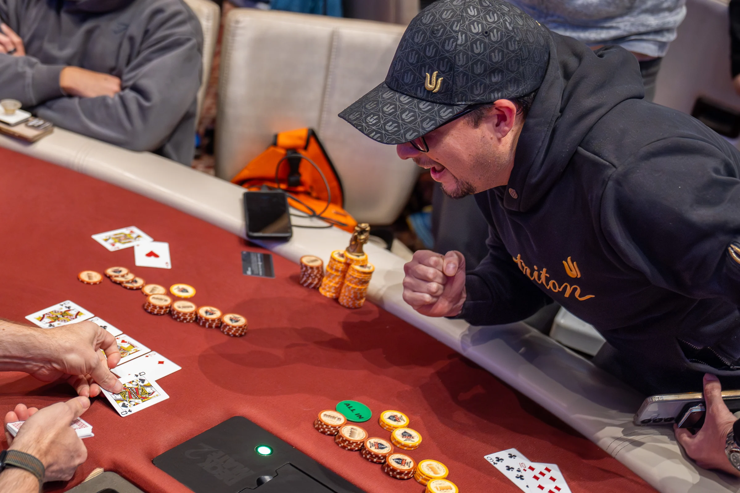 A poker player raises a fist as cards and chips are revealed across the table.