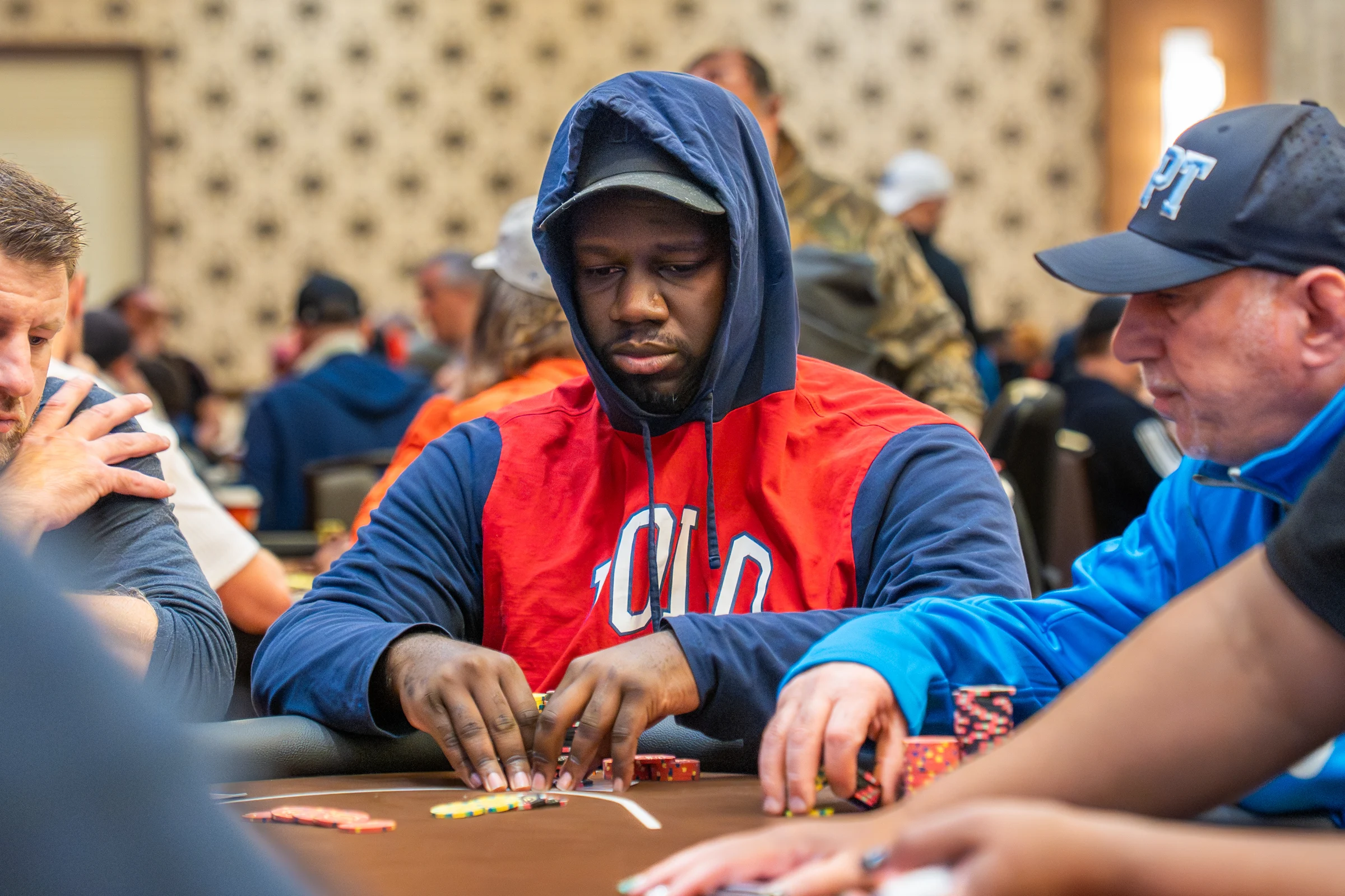 A focused poker player stacks chips at a crowded tournament table.