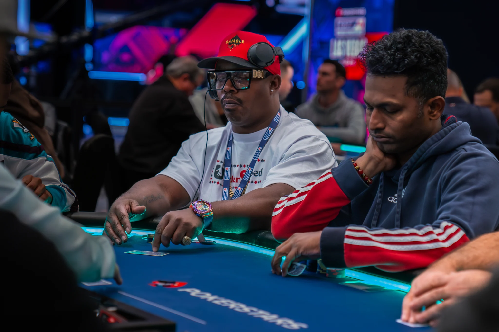 Two poker players study the action at a PokerStars table in a busy tournament room.
