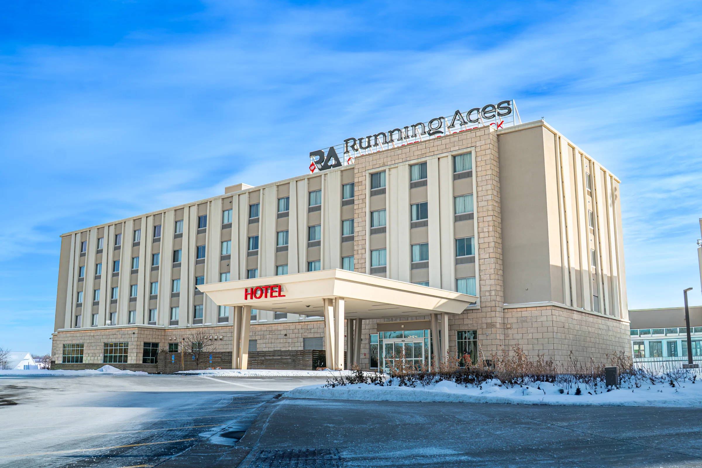 The Running Aces hotel stands under a blue winter sky beside snow-covered pavement.