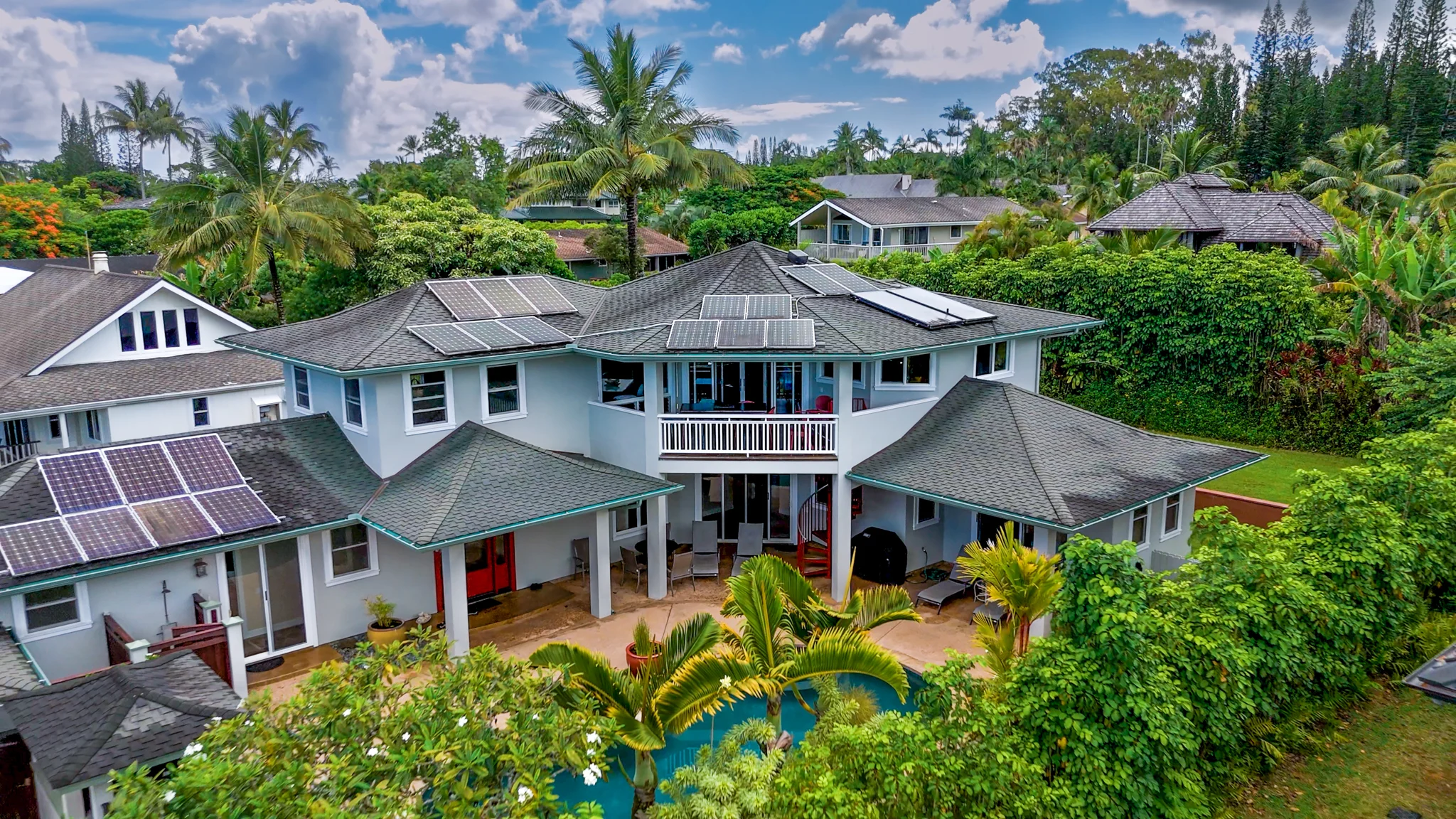Aerial view of a large tropical home with solar panels, patios, and a pool.