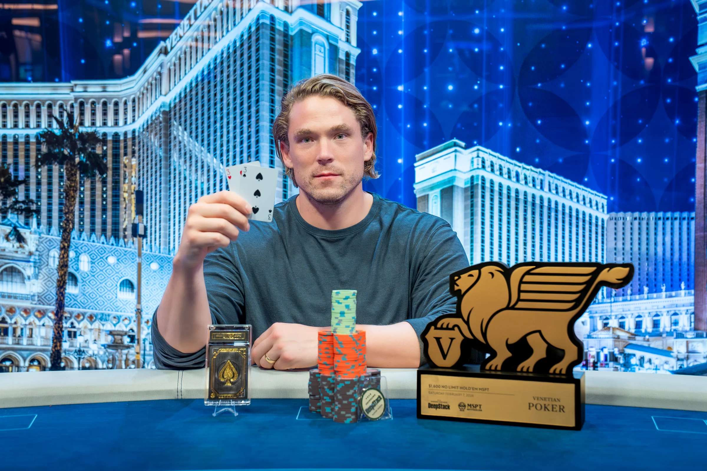 A poker tournament winner displays hole cards beside chip stacks and a Venetian Poker trophy.