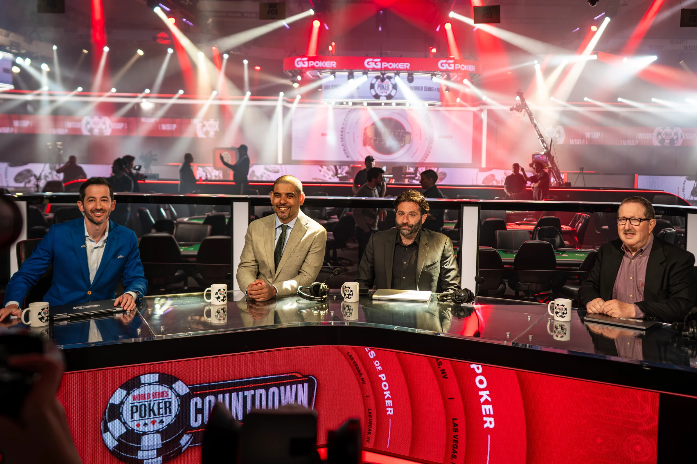 Four presenters sit at a World Series of Poker countdown desk before a brightly lit stage.