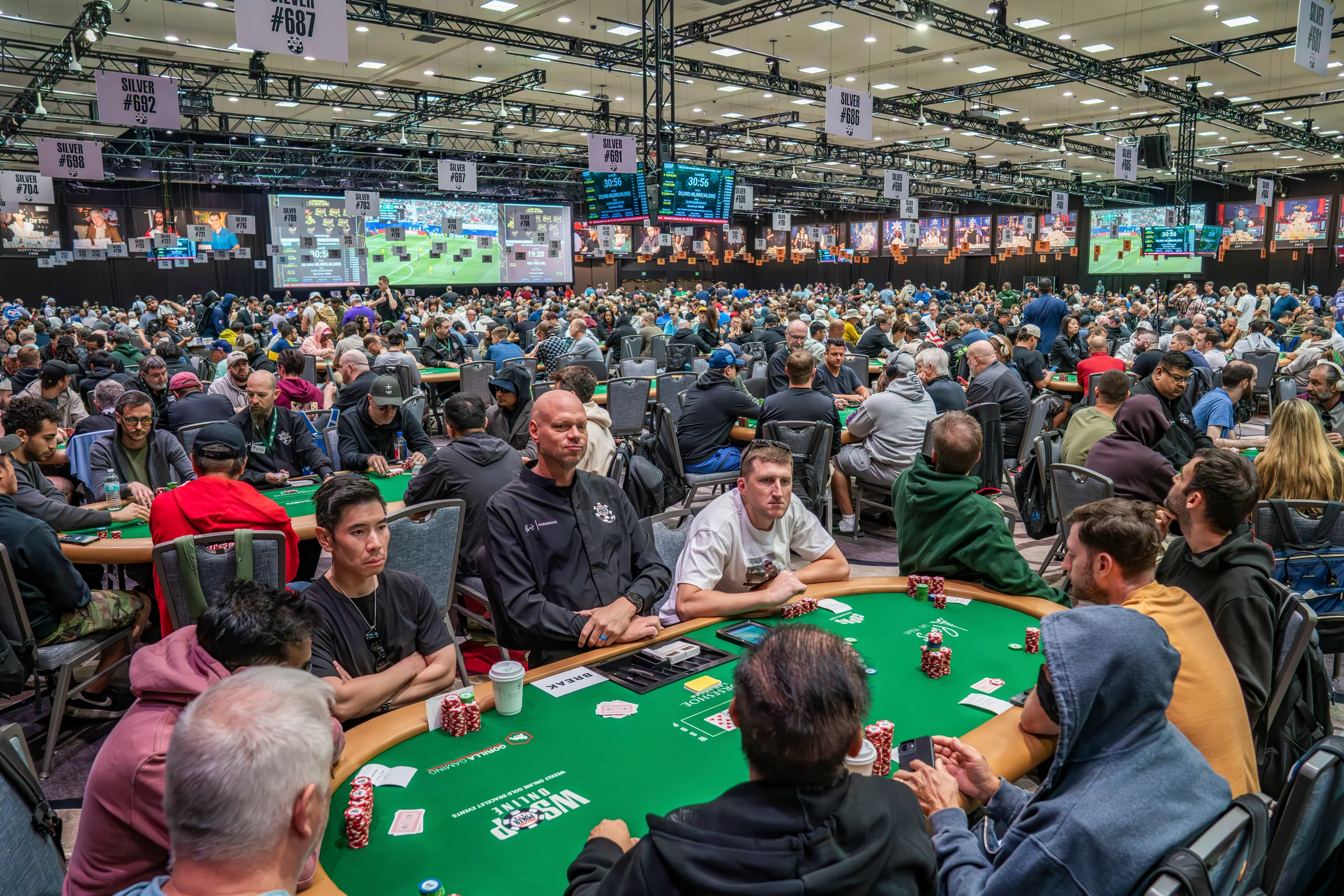 Hundreds of players fill long poker tables inside a brightly lit tournament hall.